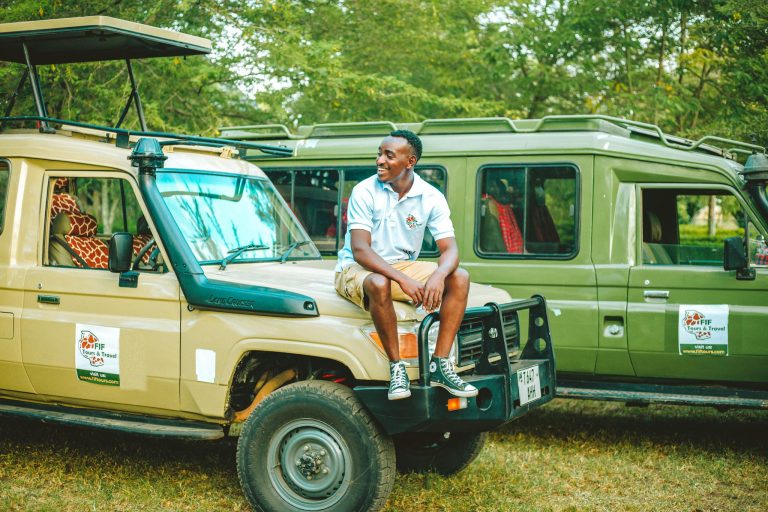 Smiling man seated on safari jeep, ready for adventure with giraffe nearby.